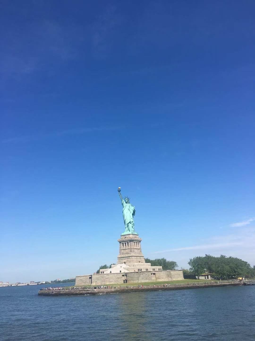 The Statue of Liberty beneath a wide blue sky, viewed from the water.